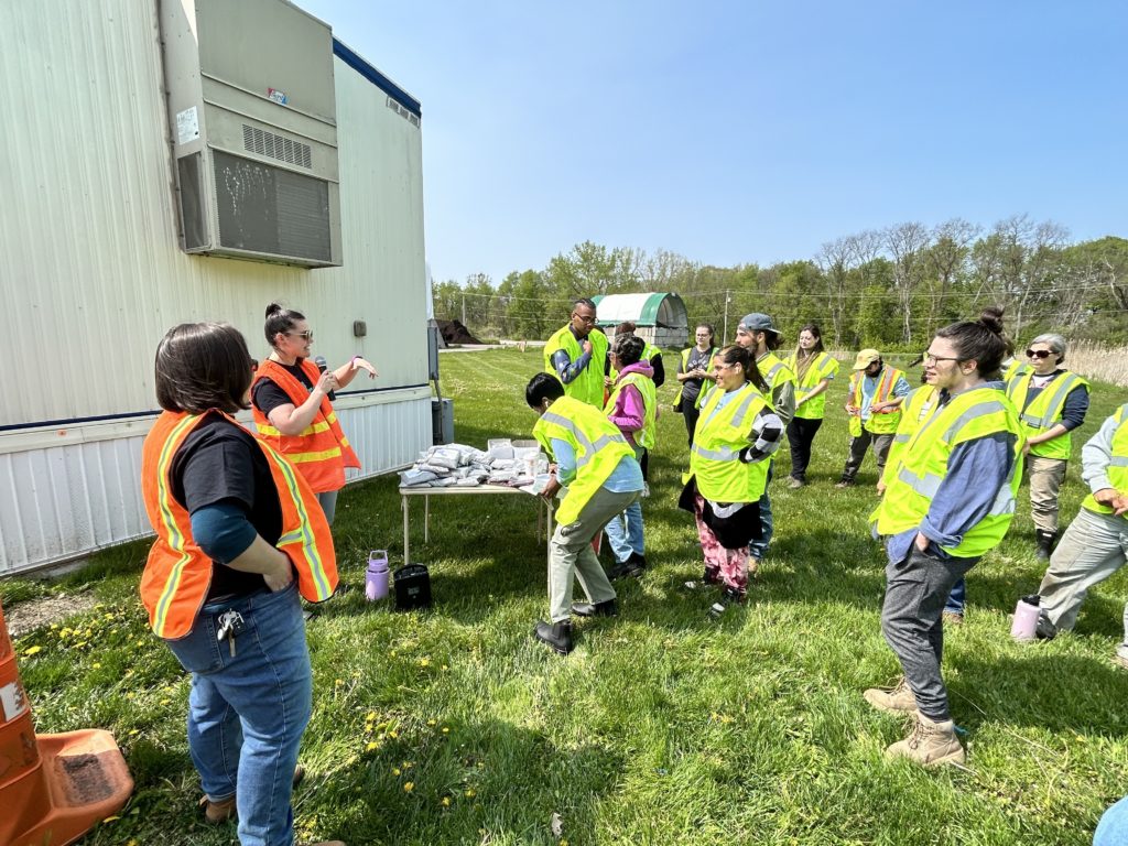 Sarah Rosenthal wears an orange vest and speaks to a large group of tour participants about the event.